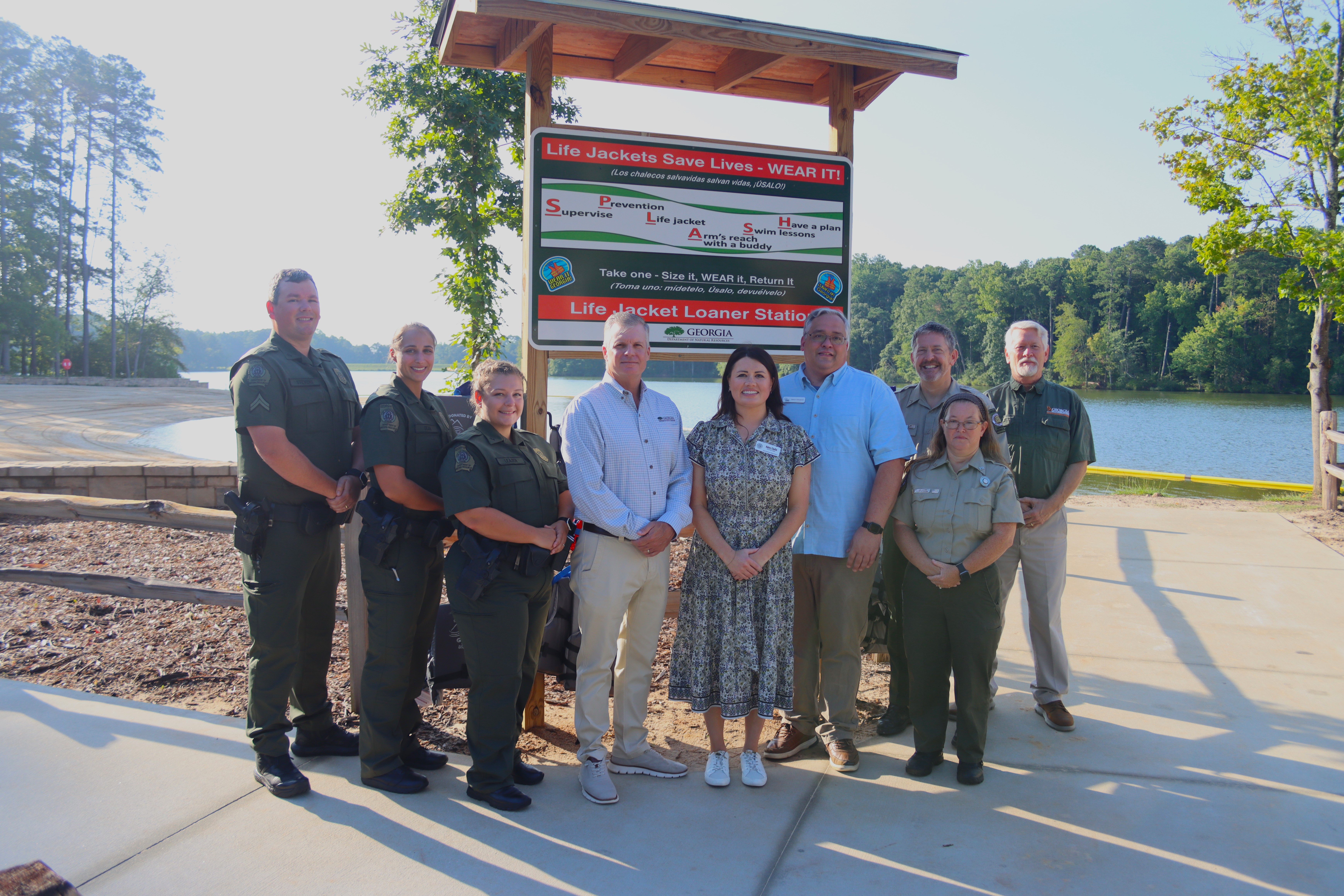Group Photo in front of life jacket loaner sign with lake in the background.